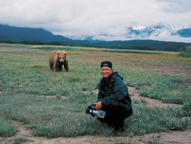 A young man poses in front of a grizzly bear.