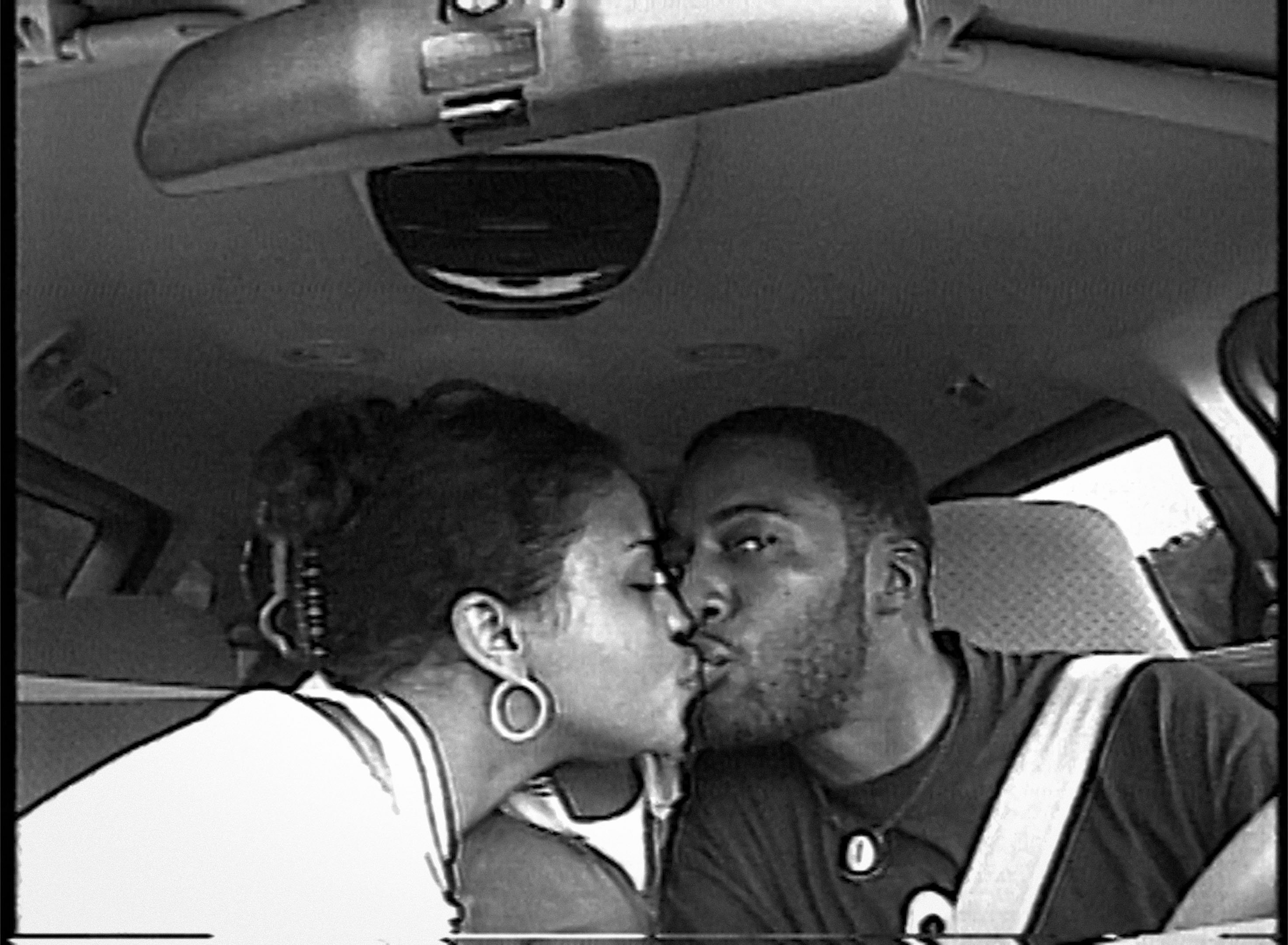 Black and white image of two people kissing in a car.