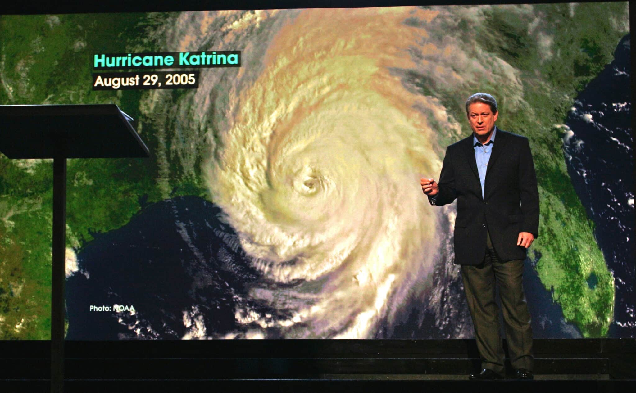 Al Gore stands in front of a giant screen of a hurricane storm radar.