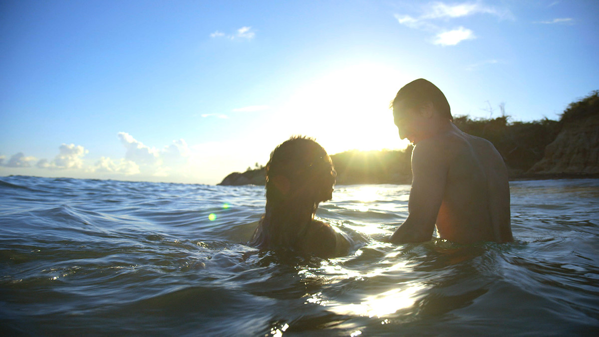 Silhouette of a man and a woman swimming in the ocean with the sun behind them 