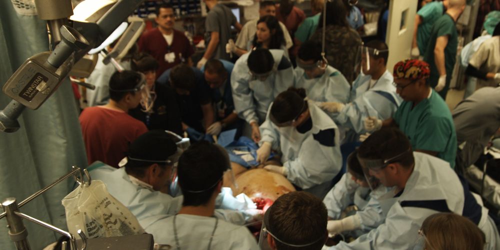 a man lays on an operating table with a large group of medical professionals around him