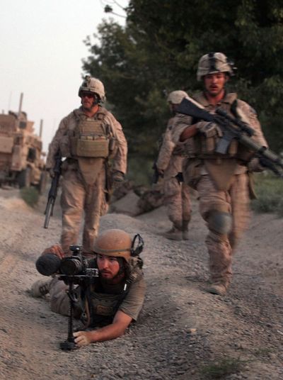 Three soldiers, two walking and one on the ground, all holding guns and wearing combat gear