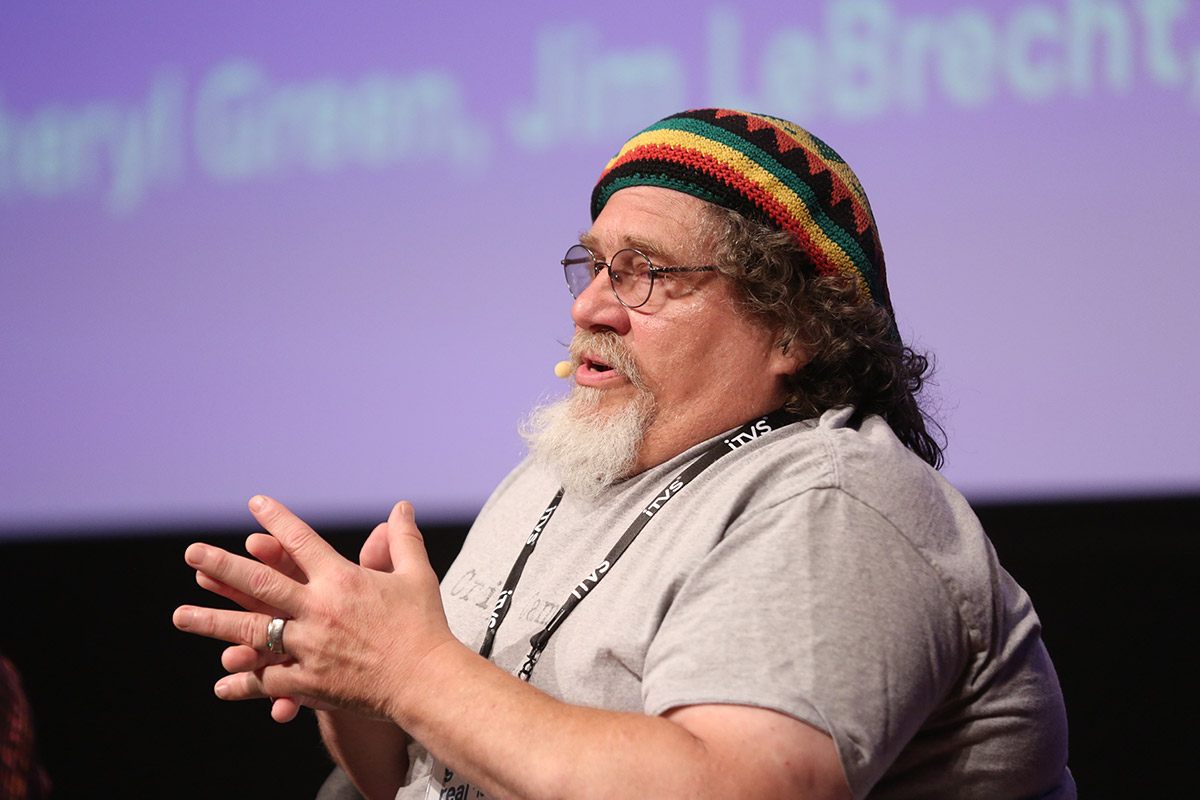 A middle aged man with curly hair and goatee speaks at a conference
