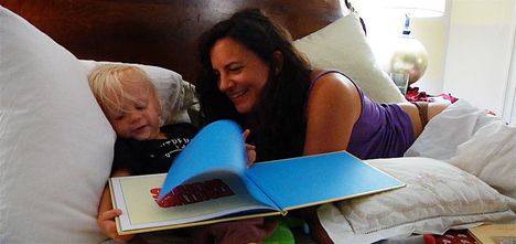 A woman and toddler lay in bed reading books