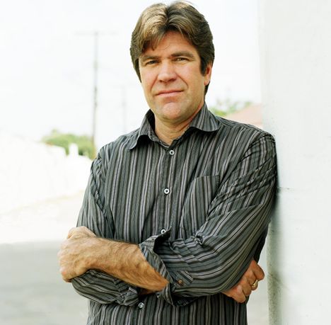 Portrait of a middle aged man in a gray striped button down, standing with his arms crossed, staring at the camera