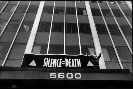 A black and white image of a building with a banner hung over the door reading "Silence = Death"