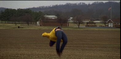 A white man in a yellow jacket jumping in the air in a backwards flip