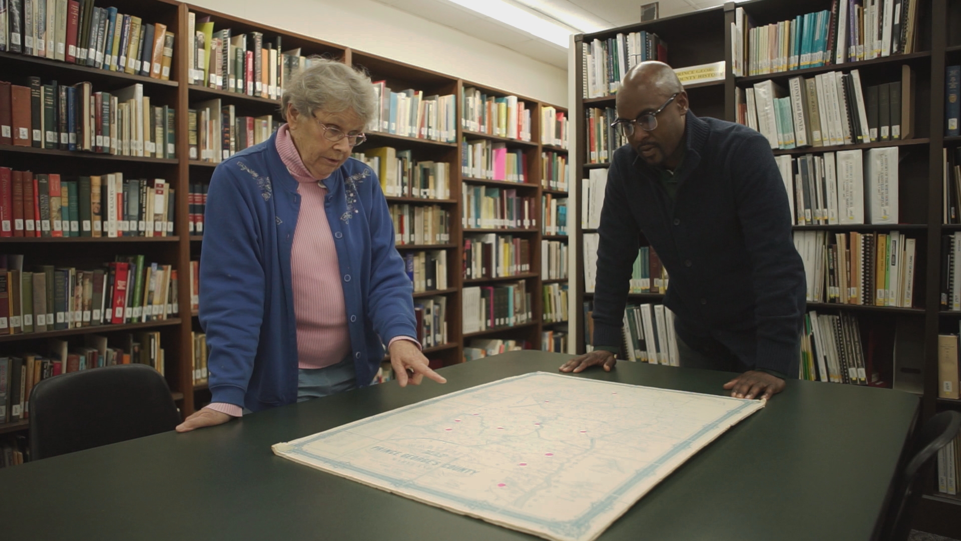 Dr. Omar Price, historian, and Susan Pearl, Librarian and Historian of Prince George's County, Maryland Historical Society are reviewing a historic 1800s map and are pointing out former Freedmen Bureau School Sites in the County. They are in the library of the Historical Society.
