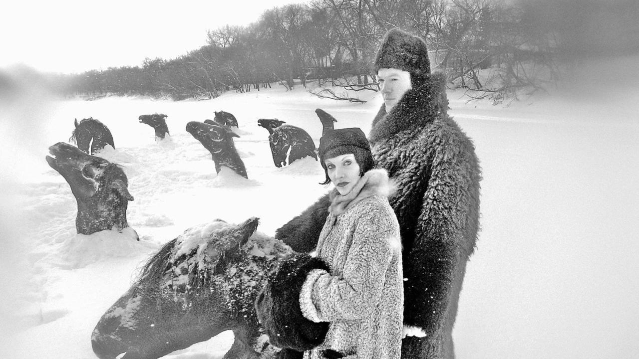 Two people in fur coats in a deep snowy field.