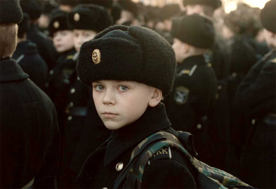 A young boy in military uniform looks at the camera.