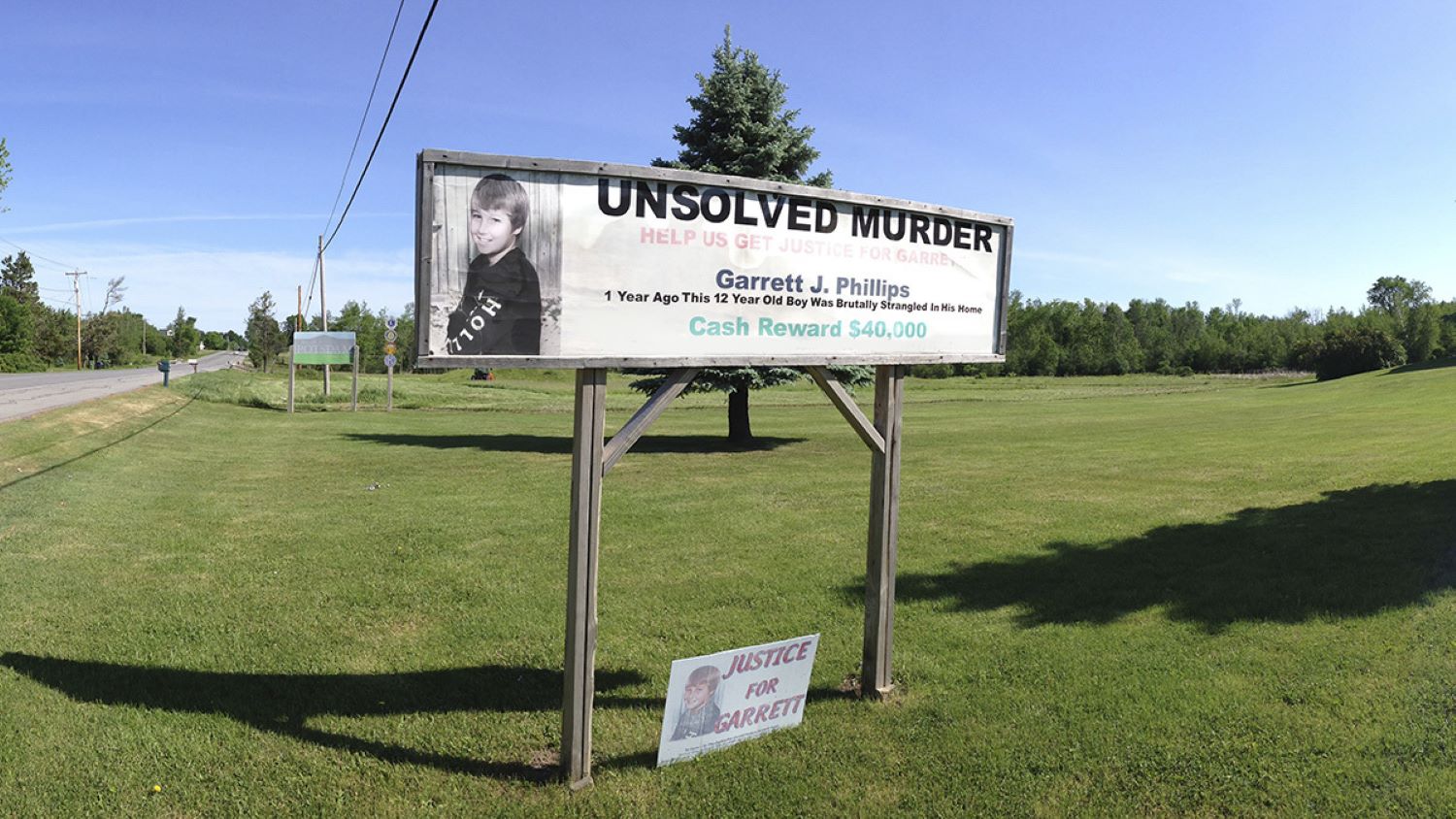 A sign on the side of the road reading "Unsolved Murder" with an image of a missing child