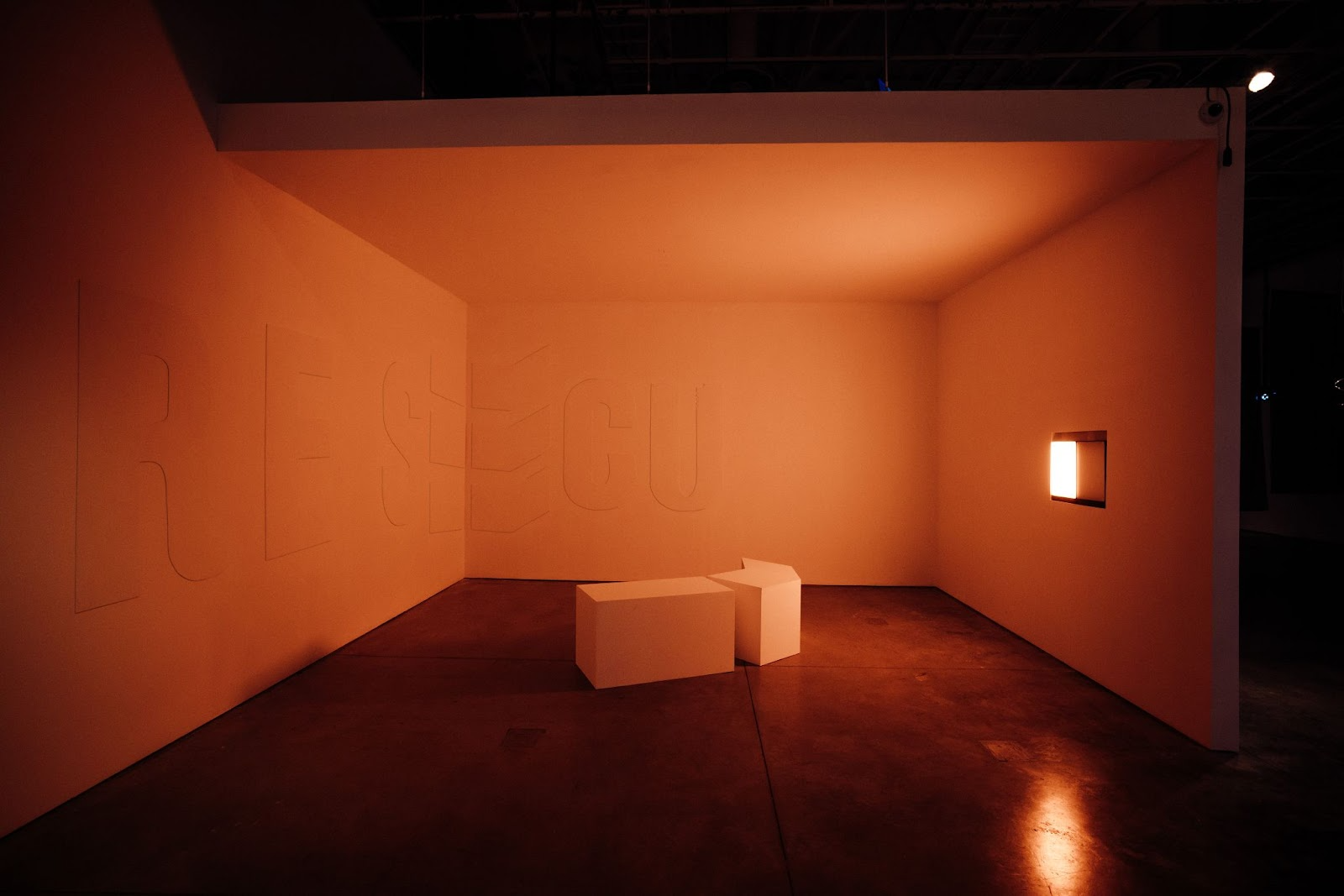 Total Running Time includes multiple works situated clockwise in a warmly lit alcove. Rescue, a plaster wall relief, and two geometric forms are positioned on the gallery floor. A niche on the rightmost wall contains two manipulated light sources, one of which creates a daylight effect.