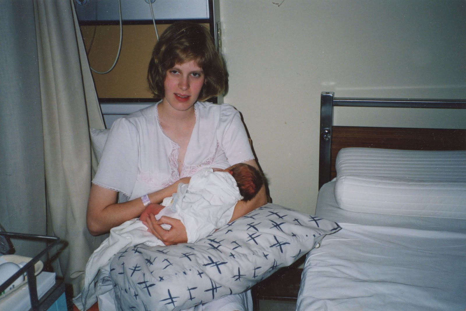 A photo of a young white woman holding a newborn baby up to her breast. She’s in a hospital room and looks slightly out of it.
