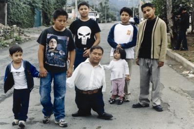 A man with no legs in a street, surrounded by six children
