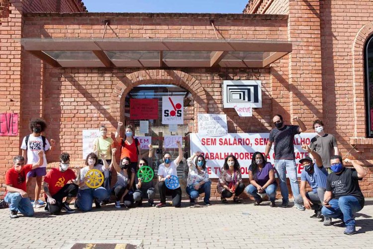 Workers stand in protest outside the Cinemateca Brasileira. They’re holding protest signs and some have their fists up in the air. Photo courtesy of Tiago Castro Gomes/Workers of Cinemateca.