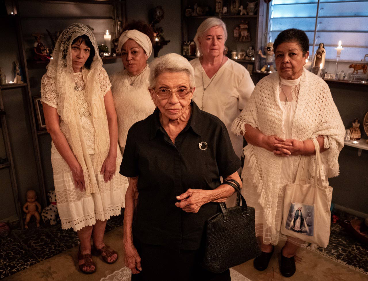 Four older women wearing all white standing behind an older woman in all black