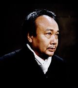 Headshot of Rithy Panh, a middle aged Asian man with short black hair, wearing a black shirt and white scarf