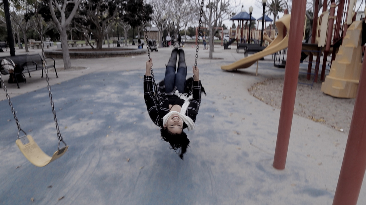From Olga 'Busy Inside.' Courtesy of WORLD Channel. A woman from the film swings on  a swing in the middle of a playground; her head is upside-down as she faces the camera.