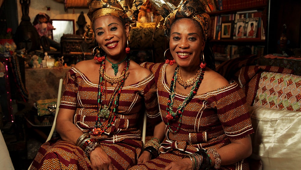 The Lijadu Sisters are a Nigerian singing duo. Taiwo and Kehinde Lijadu are two Black women wearing their traditional dress with jewelry and shiny black and golden headwraps. Image from Siji Awoyinka’s ‘Elder’s Corner: A Musical Voyage of Discovery’. Courtesy of BlackStar Film Festival.