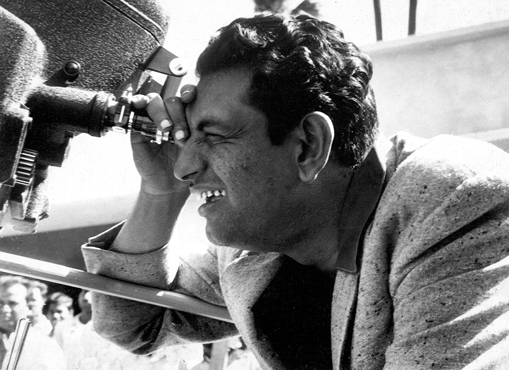 Black and white photo of Satyajit Ray looking through a camera. Courtesy Criterion Channel.