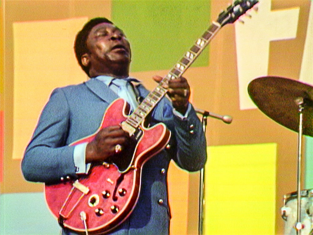 BB King, a Black man in a grey suit playing a red guitar, at the Harlem Cultural Festival. Courtesy of Searchlight Pictures.