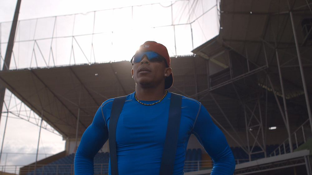 Happy Oliveros is an Afro-Latino man in a blue t-shirt with suspenders. He is wearing sunglasses and a red hat. Image from Sami Khan and Michael Gasset’s 'The Last Out.' Courtesy of Tribeca Festival