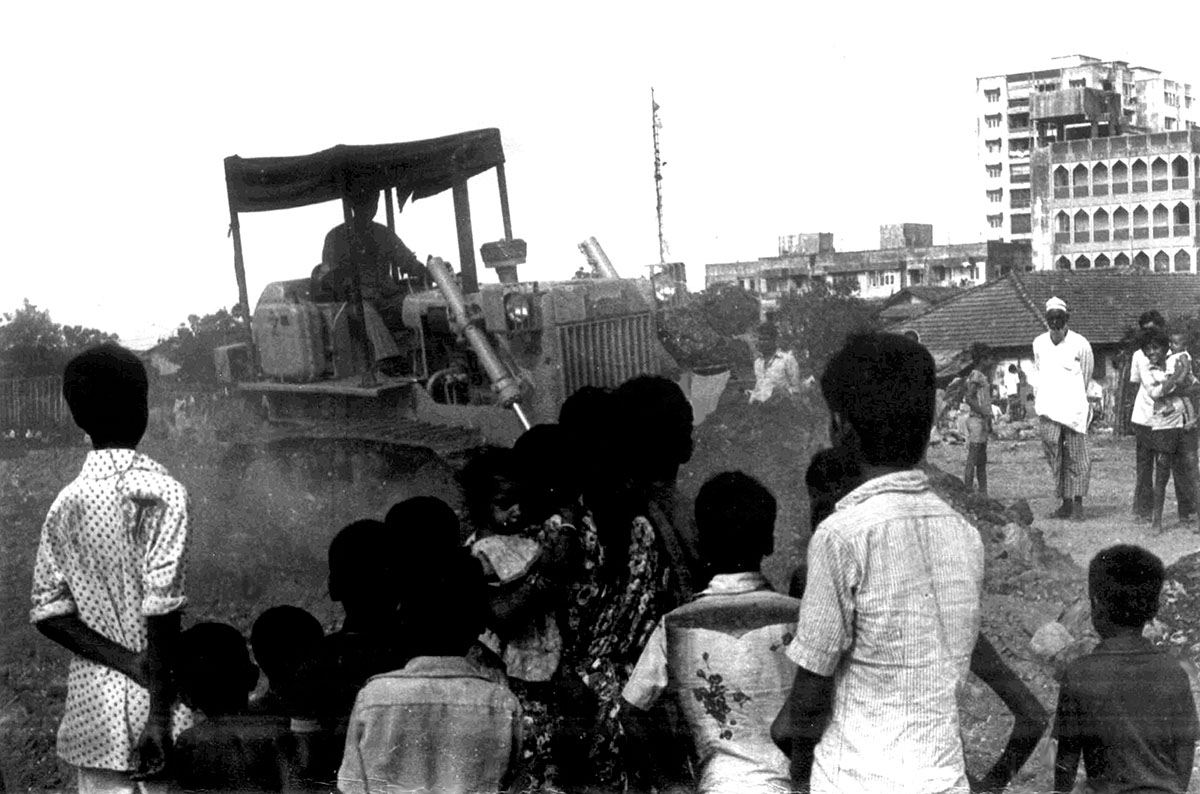 A black-and-white image of a bulldozer demolishing a slum in Mumbai, while some slum dwellers look on. Image from Anand Patwardhan’s ‘Bombay Hamara Shahar.’ Courtesy of OVID.tv