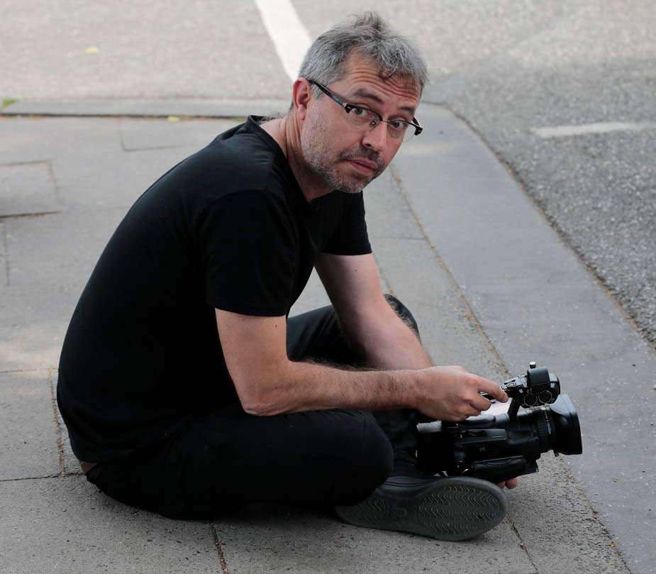 Óscar Molina is a Colombian male filmmaker seen here in a black shirt and pants, holding a video camera. Photo: Swanhild Kruckelmann. Courtesy of Óscar Molina.