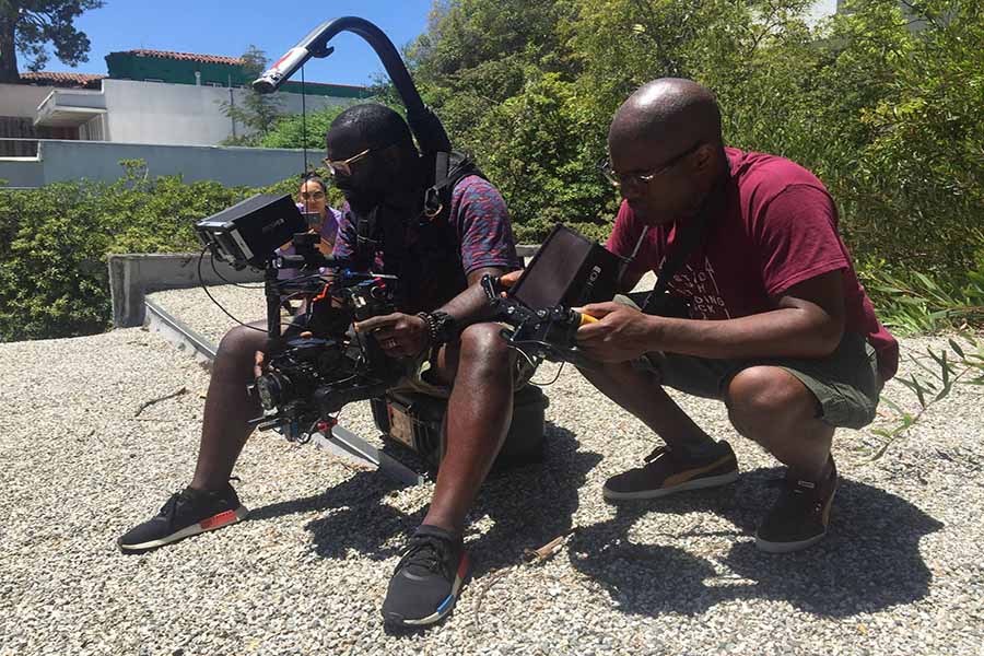 Members of the 'Ferguson Rising' crew sitting outdoors, holding camera equipment. Courtesy of Mobolaji Olambiwonnu