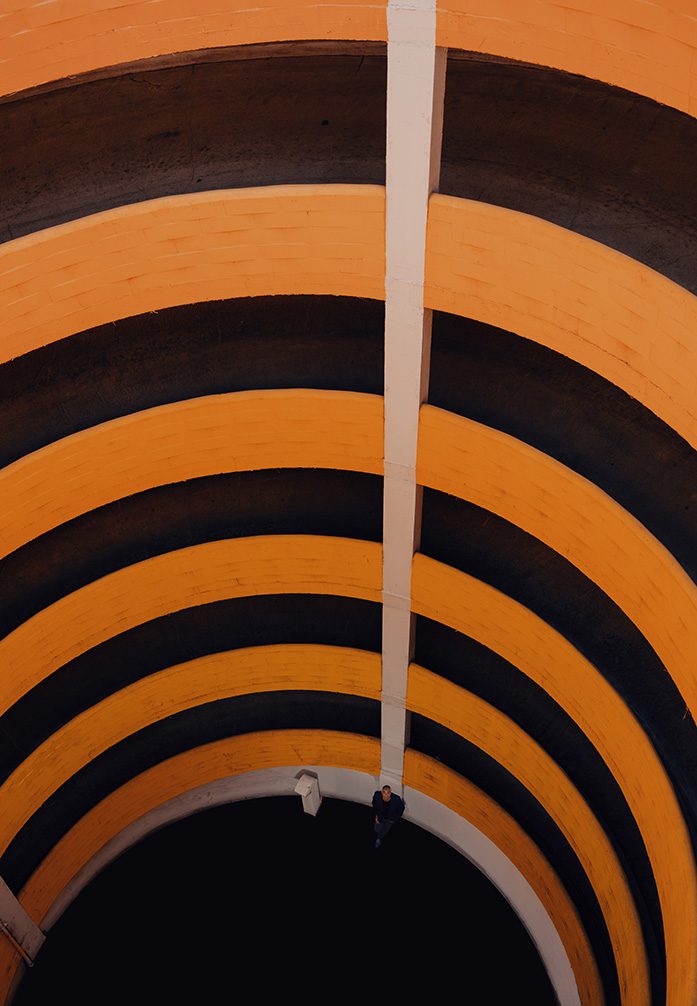Photo by Adam G Perez. Photo taken from the top of circular parking ramp that is painted in a gradient orange.