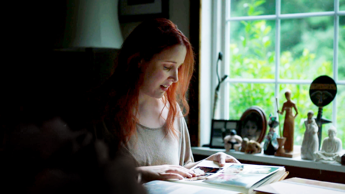 Dylan Farrow, featured in Kirby Dick and Amy Ziering's 'Allen Vs. Farrow.' Dylan is a white woman, with red hair, in her early 30s; she is sitting at a desk next to a window, and she is looking at a photo album. Courtesy of WarnerMedia