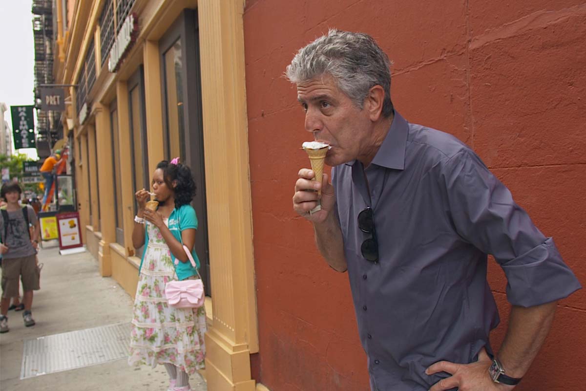 Anthony Bourdain, a white man with white hair, stands on a city sidewalk eating an ice cream cone. From Morgan Neville's  'Roadrunner.' Courtesy of Focus Features, in association with Zero Point Zero. 