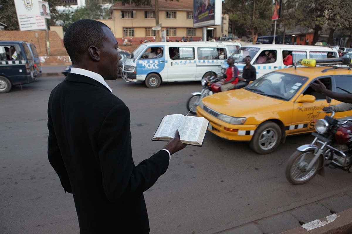 A Black male pastor reading from the Bible amidst city traffic. From Roger Ross Williams' 'God Loves Uganda.' Photo by  Derek Wiesehahn.