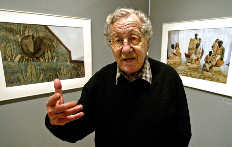 An older man is caught mid conversation, standing between two photos.