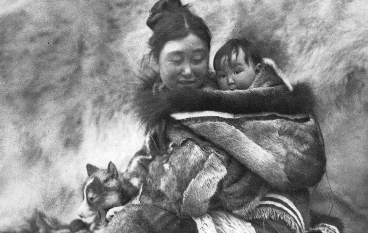 A woman smiles while looking towards the baby she's carrying on her back. From Robert Flaherty's 'Nanook of the North' (1922).