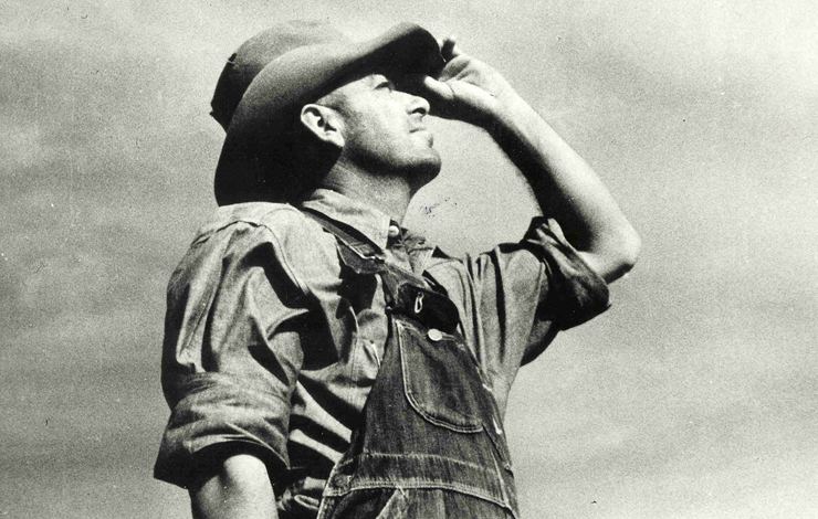 A man in overalls looks upward while holding his hat on his head from Pare Lorentz's 'The Plow that Broke the Plains.'(1936)