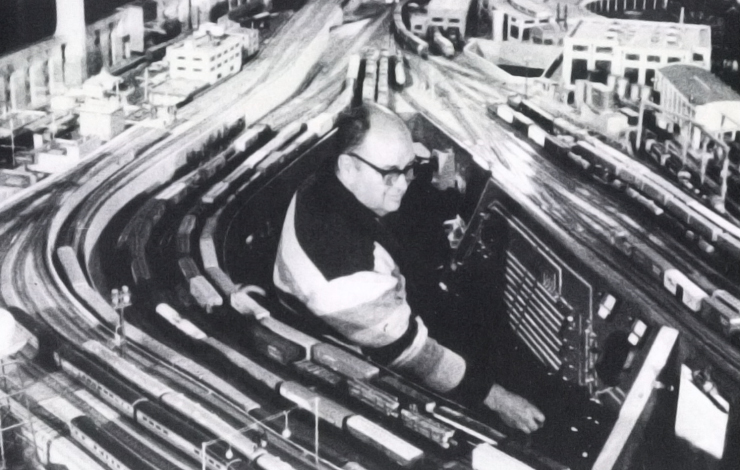 A man sits in the middle of an intricate model rail road track. From 'Routine Pleasures.'