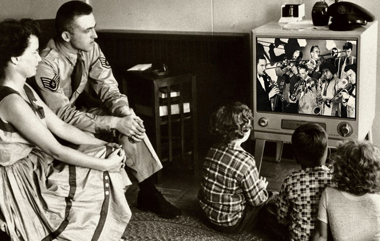 A family sits around watching their box T.V. 