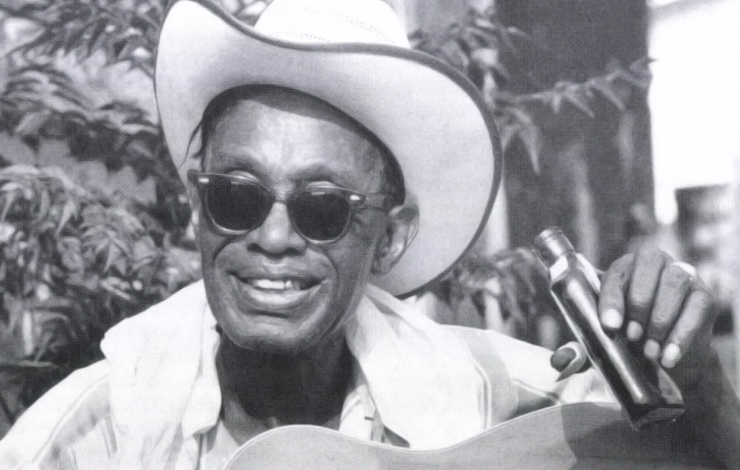 A Black man wearing a cowboy hat holds a flask; a film still from 'The Blues Accordin' to Lightnin' Hopkins.'