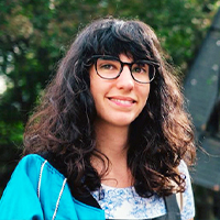 A woman with long wavy black hair with bangs. Wearing glasses. 