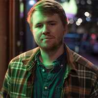 Blonde and lightly bearded, draped in city light, wrapped in flannel as always. 