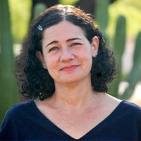 A white woman with curly, dark hair in front of cactus plants.