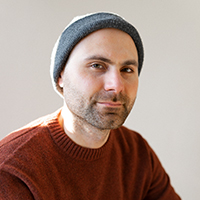 A man with light skin with black facial hair wearing a blue beanie