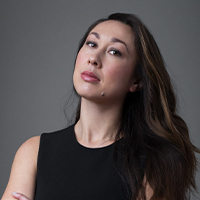 A woman with brown hair, wearing a black sleeveless top, with her arms crossed.