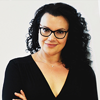 A woman with light skin, long black hair and round black glasses.