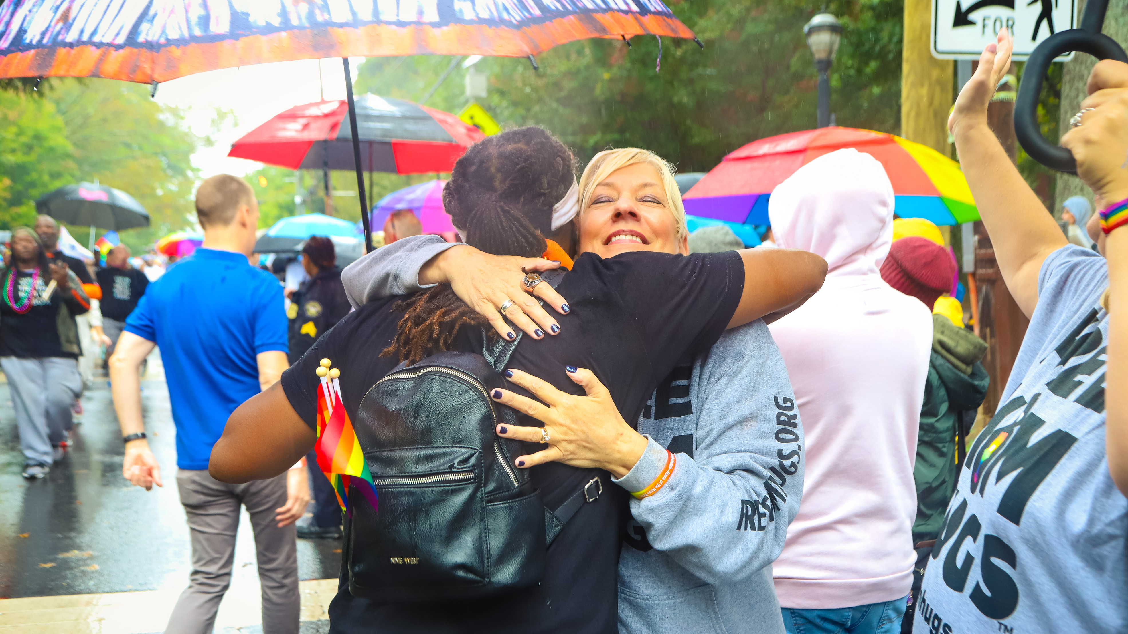  A mother from the mama bears movement hugs a person wearing a black backpack with rainbow pride flags hanging from it during a Pride celebration. Photo courtesy of 'Mama Bears' .