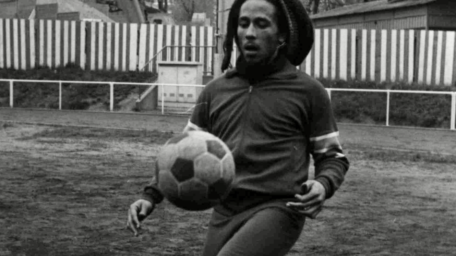 Reggae legend and football fan Bob Marley, in dreadlocks and beard and wearing a dark jersey, dribbles a football. From ‘Legacy: Rhythm of the Game.