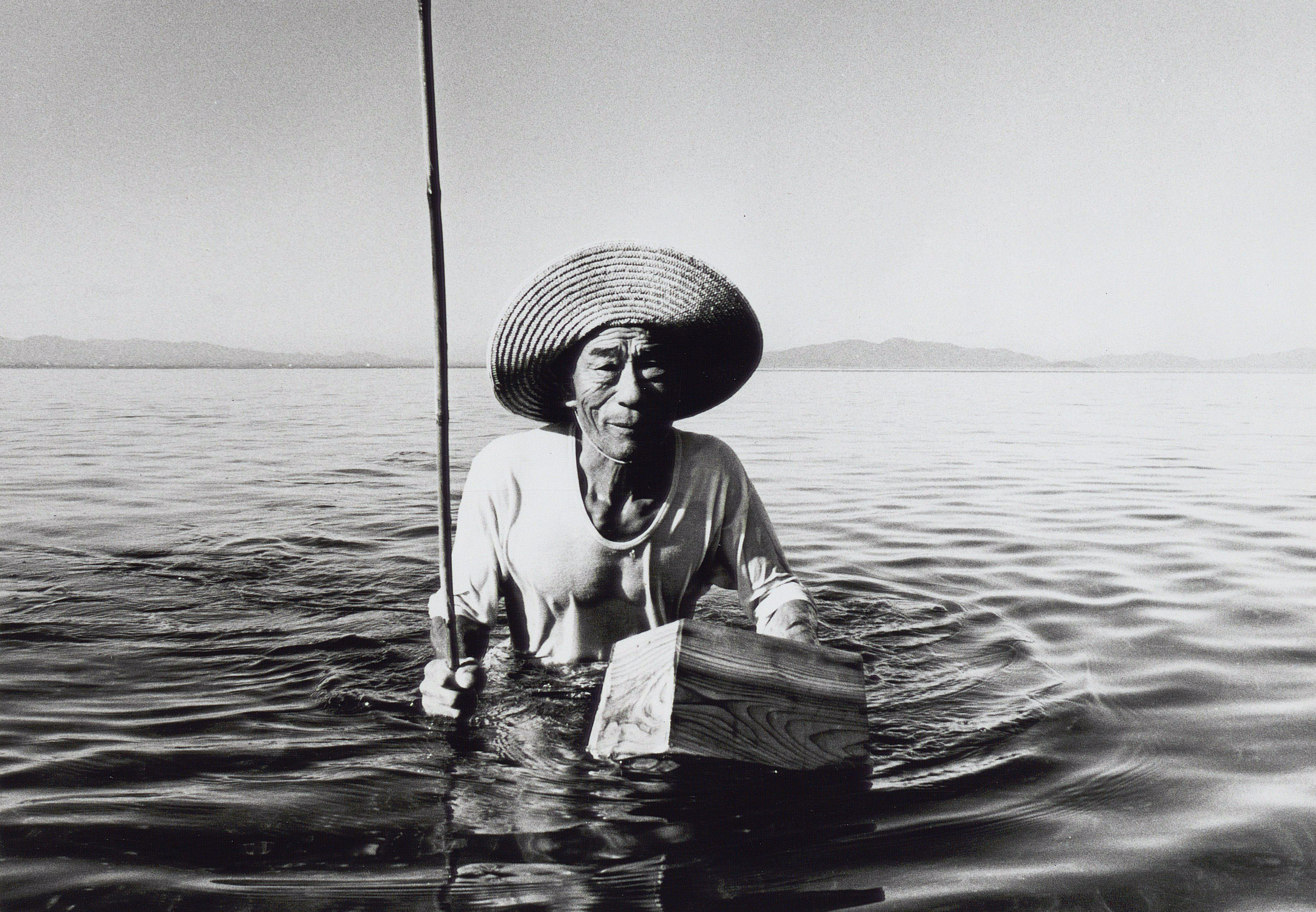 A Japanese fisherman man wearing a hat to shade himself from the sun wades through water while fishing. Photo courtesy of Siglo, Inc. 
