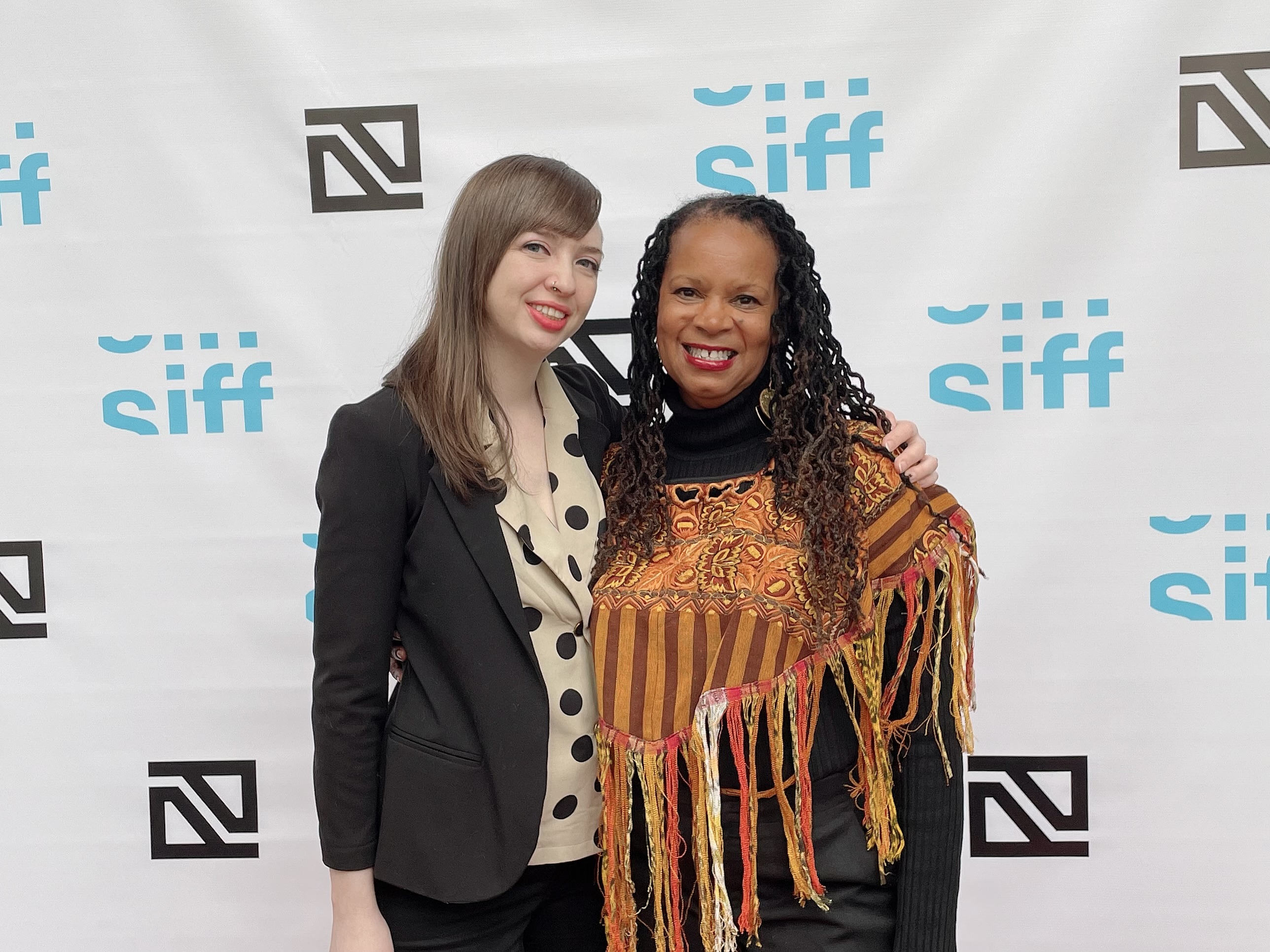 Daresha Kyi (right), a black woman with dreadlocks and a brown striped shawl, and Laura Tatham (left), a white woman with a black blazer and polka-dot shirt, pose together at Seattle International Film Festival. Photo courtesy of Daresha Kyi. 