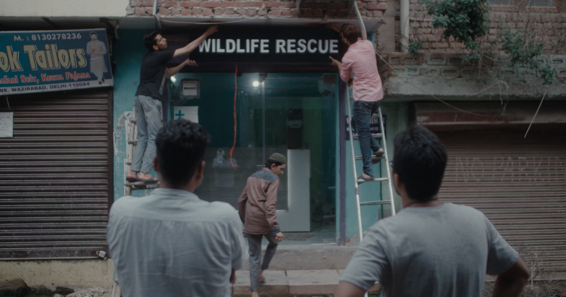 Two men watch as a ‘Wildlife Rescue’ sign is installed outside of a brick building. All images from Shaunak Sen’s ‘All That Breathes’. Courtesy of Cinetic Media.